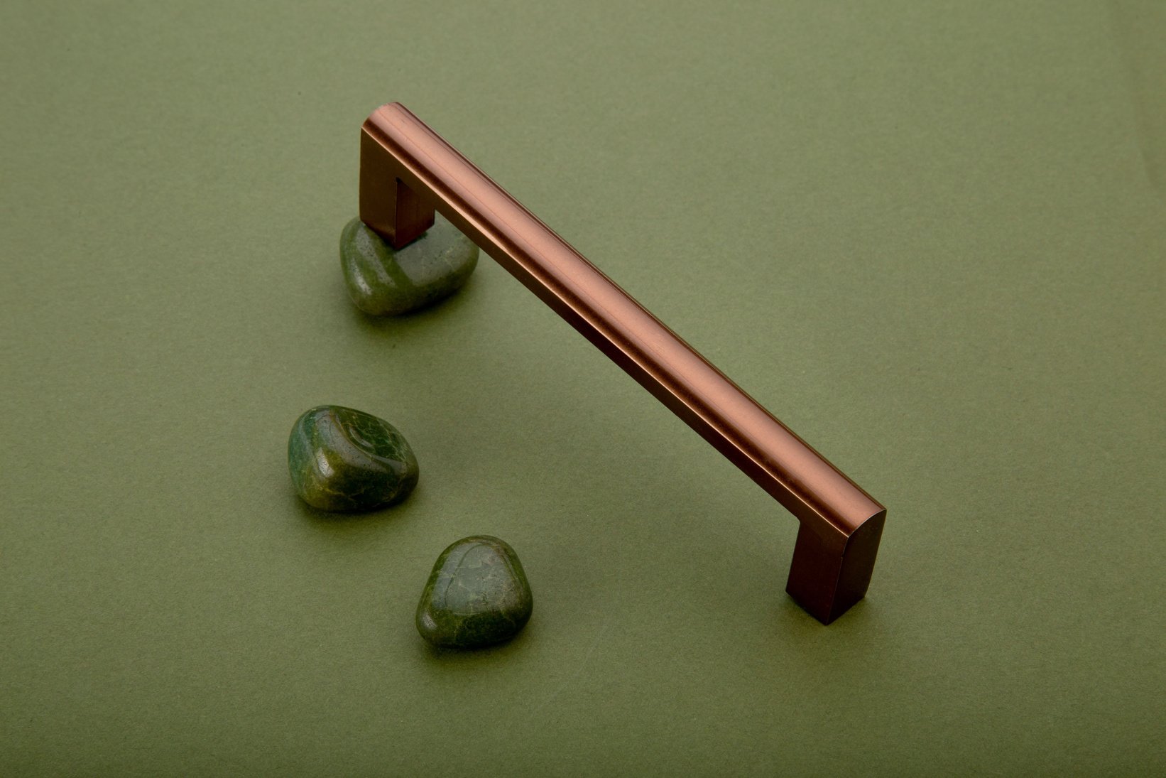 Shiny copper pull handles and green natural stones on green surface